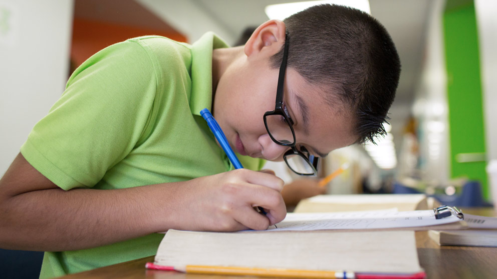 Student in green shirt with glasses reading a text book.