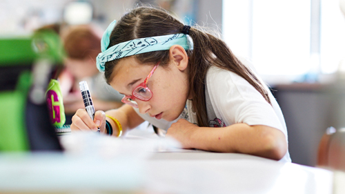 Student with headband working hard on a project at her desk.