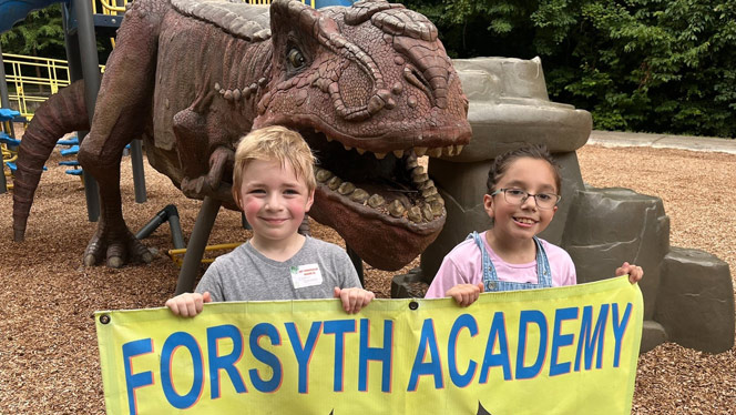 K-8 School in Winston-Salem NC: Students hold Forsyth banner in front of dinosaur.