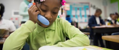 Buffalo United Charter School, K-8 School in Buffalo NY: girl sitting at desk reading a book and using a reading phone.