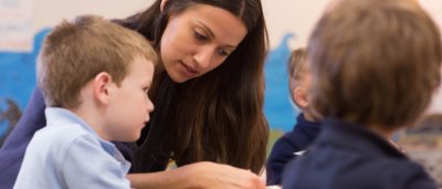 K-8 School in Commerce City: Teacher helping students at desk.