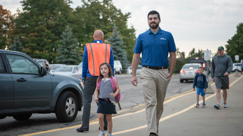 Parent walking their child through the school parking lot.