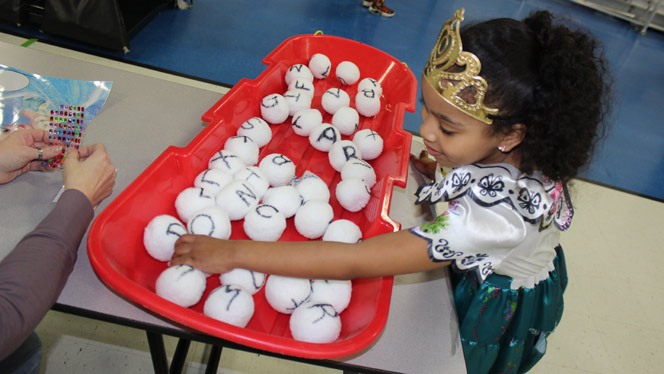 K-12 School in Waterford: Student dressed as a princess choosing a ball out of a bucket with a letter written on it.